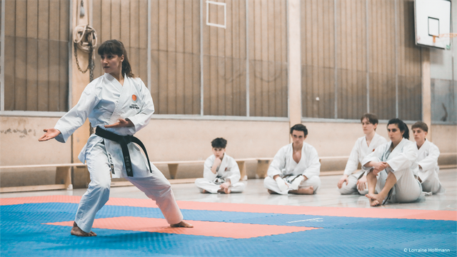 Vice champion Leonie Diffené in the category 'kata' and PhD student at the WiSo Faculty in the area of Demography and Social Inequality. The photos were taken during her karate training. She is shown in different training positions. In this shot Leonie is seemingly presenting a routine to other people, which are sitting in the background, watching her.