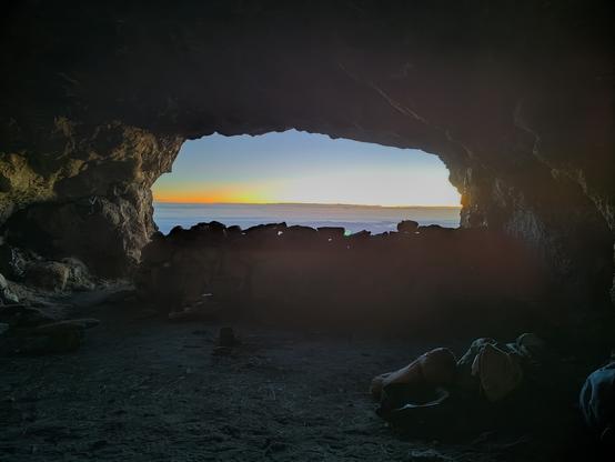 View from a basalt cave acts like a window with the dark sides of the cave contrasting with the light and colours of a sunrise on the horizon