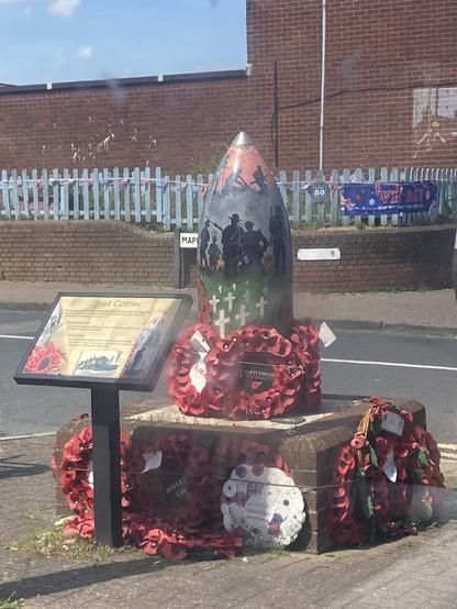 A war memorial made out of an artillery shell, with an image of are brave boys painted on it, and surrounded by poppy wreaths.