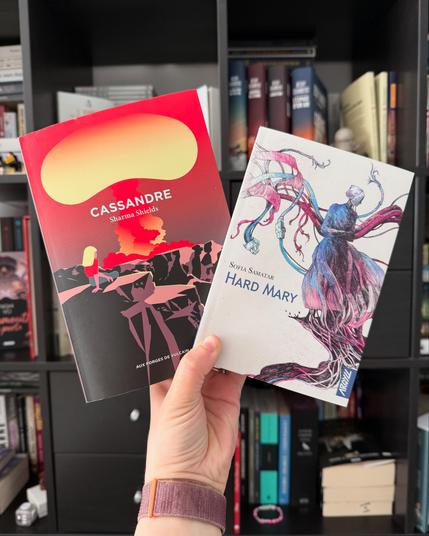 Livre pris en photo devant une bibliothèque. 
La couverture d’Hard Mary montre une femme en tenue Amish d’où s’échappent des câbles et prises.
La couverture de Cassandre montre une femme de dos, assise sur une montagne, regardant un nuage atomique au loin.
