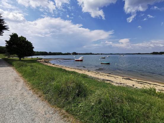 Un paysage de bord de mer avec un chemin de cailloux au premier plan, une petite plage au second plan et la mer en arrière-plan.