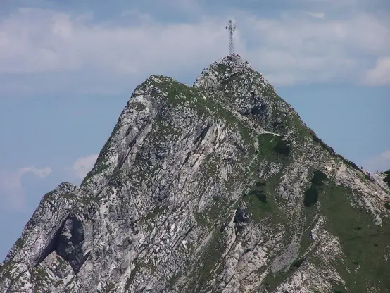 The image shows a mountain peak with rocky surfaces and green vegetation. At the top of the peak, there's a cross or similar structure. The sky is partly cloudy, providing a scenic backdrop. The overall atmosphere suggests a natural, mountainous environment, likely popular for hiking or sightseeing.

Image Credits: Wikimedia / Opioła Jerzy / CC BY 2.5