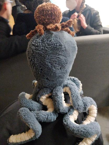 Une petite peluche de poulpe brun sur la tême d’une plusse grande peluche de poulpe bleu