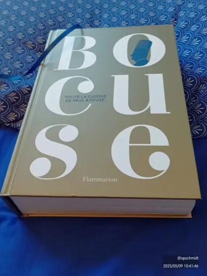 Livre de cuisine posé sur un tissu bleu. La couverture est sobre le titre couvre toute la couverture BO en haut, CU au milieu et SE en bas sur un fond beige cuivré. Le livre est vu en perspective de manière à montrer son épaisseur.