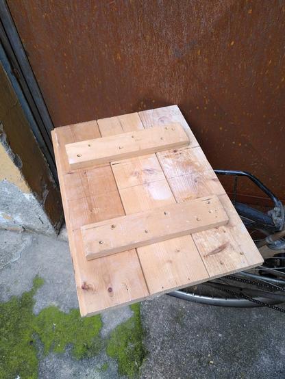 The same board turned upside down shows two smaller pieces of wood perpendicular to the three planks. These serve both to keep the planks together as well as keeping everything snug on the bicycle rack.