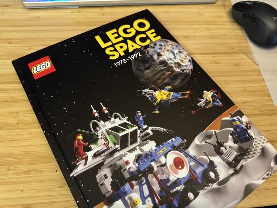 Photo of a hardcover book on a desk: “LEGO Space: 1978–1972”, published in 2023. The scene on the cover is various vintage LEGO Space sets staged against a space background.