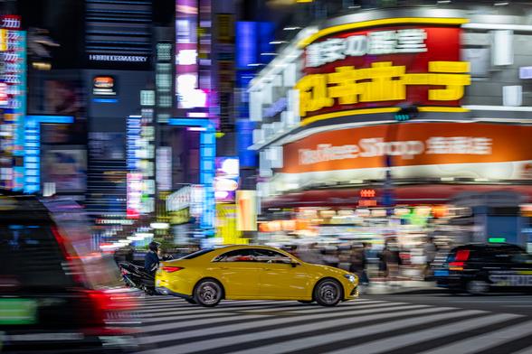 Panning shot of a yellow sport car speeding on a busy street at night in Shinjuku, Tokyo, Japan, on a background of skyscrappers illuminated by neon lighting.