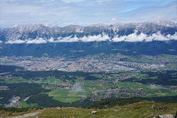 Blick auf Innsbruck vom Zirbenweg aus mit Gebirgskette dahinter. Ein Wolkenband zieht sich durchs Bild.