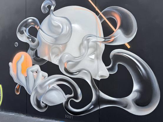 Street art of the top head of a head, in stak white with orange lighting. Water is swirling around it, and below it is a disembodied hand holding an orange egg.