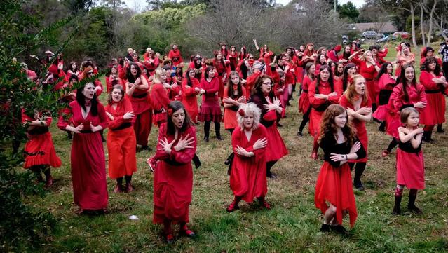 Check for local events near you. 
In a grassy winter field surrounded by green trees, people of all ages dance in formation to Kate Bush music, all wearing long red dresses with a black sash. Photo: David Brazil