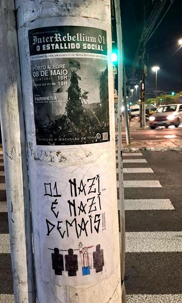 Foto de um cartaz de divulgação da exibição do Interrebellium colada em um posta numa rua.

Abaixo há outro cartaz onde se lê: 01 nazi é nazi demais!