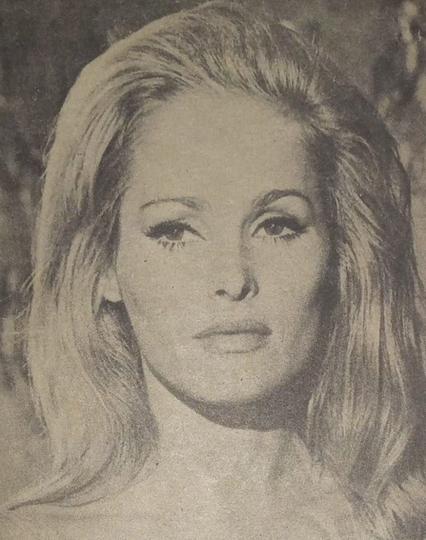 Retrato en blanco y negro de una mujer con cabello largo y rubio, luciendo una blusa de tirantes y mirando hacia la cámara con una expresión seria.