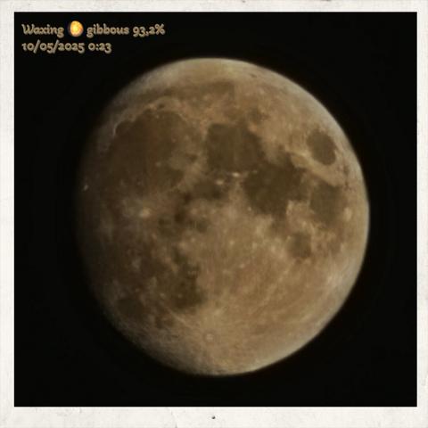 Alt text by Bing:
A high-resolution photograph of the Moon in its waxing gibbous phase, with 93.2% of its surface illuminated. The Moon's rugged terrain is prominently visible, displaying craters, basins, and flat lunar maria. Shadows cast by the sunlight accentuate the depth and contours of the lunar surface. The illuminated portion contrasts sharply against the dark, shadowed region, emphasizing the spherical nature of the Moon. In the upper left corner, a decorative font presents information: "Waxing gibbous 93.2% 10/05/2025 0:23," indicating the Moon’s phase, illumination percentage, and the date and time of the observation. The deep black background isolates the celestial body, enhancing its striking visibility.