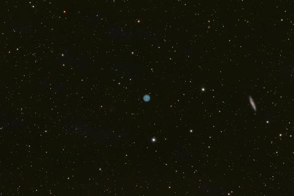 A field of stars with a small, blue globe of gas with a red outer fringe at the center of the frame (M97), and a side-on view of a spiral galaxy to the right (M108)