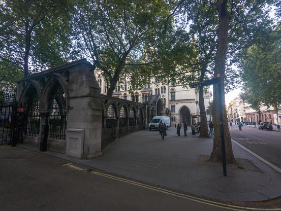 A fingerpost direction sign saying 'River Thames' and 'Temple' (latter with a London Underground icon) is pointing to a stone and iron wall, part of a large building, and with a sign saying 'LSE' attached to a gate