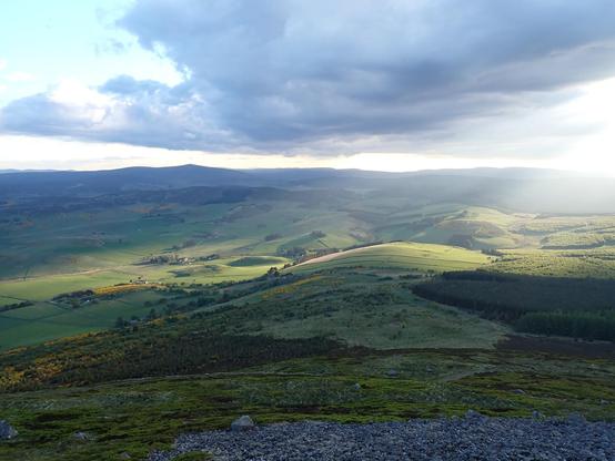 View from the top of Tap o' Noth. Evening time now. The walls of the hillfort to the sunlit fields and beyond to the bigger hills.