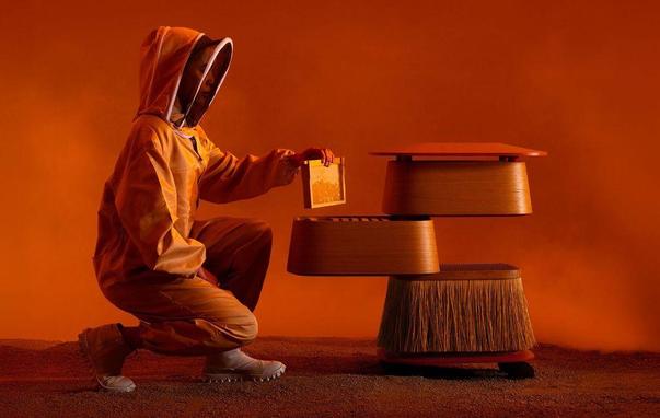 A person in an orange suit kneels beside a stylized futuristic beehive, holding a panel against a vibrant orange background.
