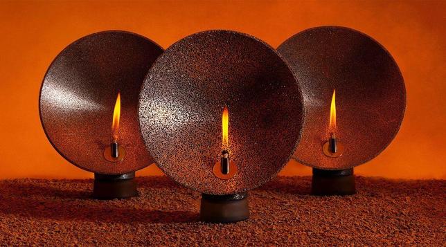 Three decorative oil lamps with flames, set against an orange backdrop and brown textured surface, creating a warm ambiance.