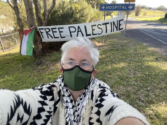 Masked woman stands in front of a Free Palestine sign at Bega