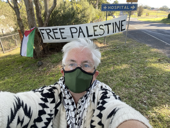 Masked woman stands in front of a Free Palestine sign at Bega