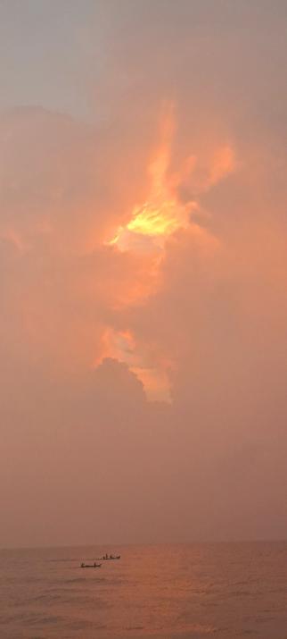 Two fishermen boats in the ocean during dawn today. Orange cloudy skies beckoning them.