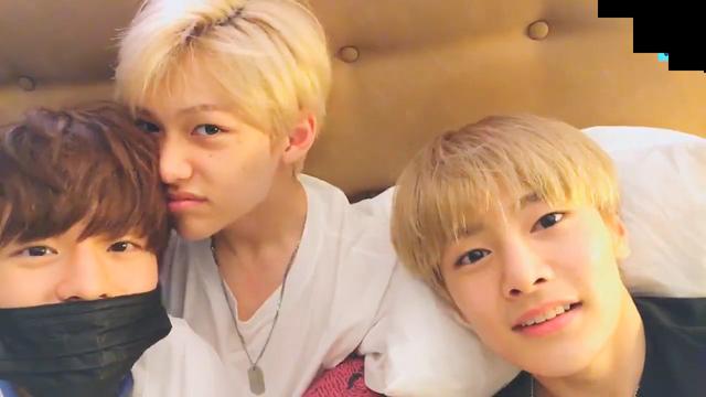 Seungmin, Felix and I.N in I.N's bed, looking at the camera. Felix's face is turned towards Seungmin's head, possibly in an attempt to kiss, sniff his hair, or something similar.
