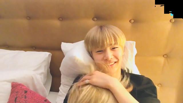 I.N in bed with the top of Felix's head visible on I.N's chest. I.N is smiling into the camera and ruffling Felix's hair.