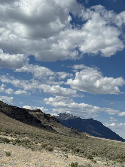Mountains in blue and grown, the farthest one snow-streaked. Wild clouds in blue sky.