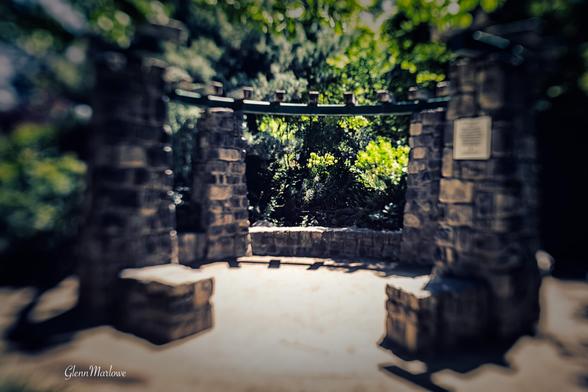 A stone structure with pillars and a horizontal beam is surrounded by lush greenery. The image has a soft focus, creating a dreamy atmosphere.