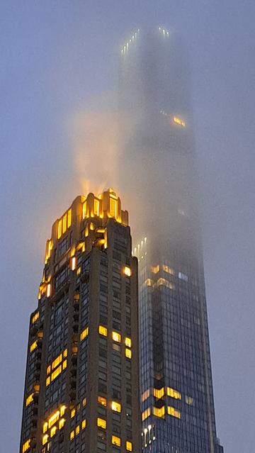 Night shot of the tops of two sky scrapers, fog obscures the top of the taller one.