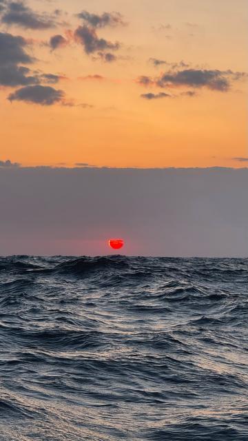 Eine tiefrote Sonne über den Wellen. Sie geht in einem Vorhang aus diesigen Wolken auf.