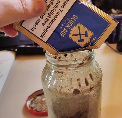 Eine Nachfüllpackung Schnupftabak wird in ein leeres Marmeladenglas gefüllt, um ihn mit einer anderen Sorte zu mischen.