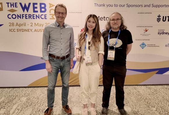 A picture of three persons in a row. From left to right: Steffen Staab, Yunjie He, and Daniel Hernández. The picture is inside the International Conference Center in Sydney. In the background there is a big panel printed with the conference logo, and sponsor names.