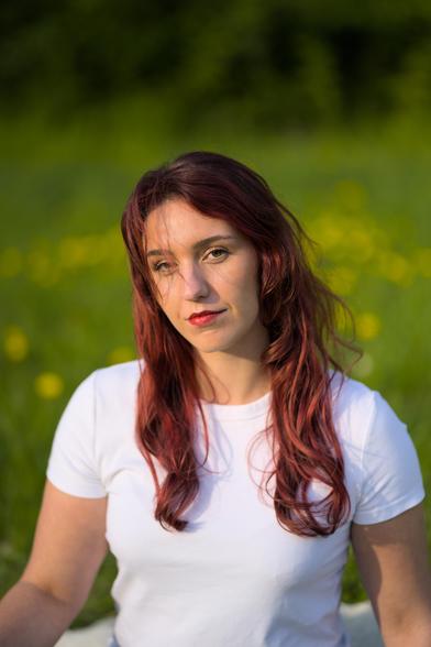 Eine rothaarige Frau sitzt in der Sommersonne auf einer grünen Wiese.