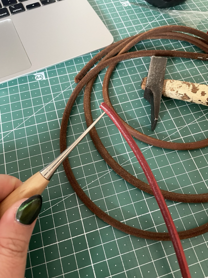An awl perforates the end of a new leather belt for the machine. In the back there is the old belt and a hammer.