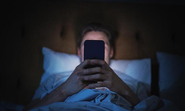 Hombre anónimo usa teléfono inteligente en la cama en casa por la noche. (Getty Images)