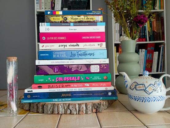 Une photo des livres cités empilés les uns sur les autres sur une table avec à côté un bouquet de fausses fleurs, une théière décorée et un petit tube de fleurs séchées.