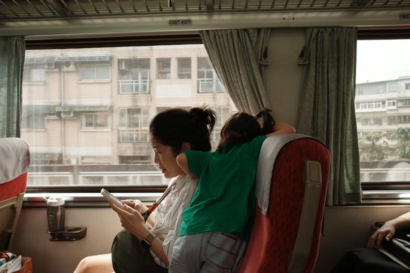 On a strain, a young woman types on her phone, as her daughter looks over her shoulder