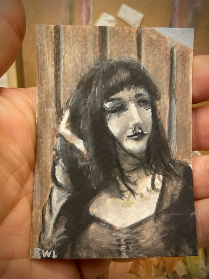 A miniature portrait painting, held in the palm of a hand. A goth woman standing in bright sun in front of a wooden fence.