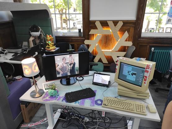 An overhead view of the Birkenhack stall at Wirral Makefest 2025. There is a Nix logo in the middle, a classic Macintosh LCIII on the right, and a lithophane lamp to the left, as well as a bulbasaur planter.