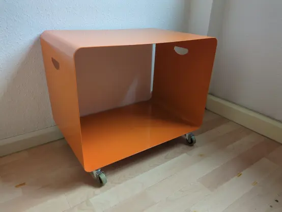 In einer Zimmerecke steht ein orangefarbenes Board, 60 cm breit, 40 cm tief und 51 cm hoch, und wartet auf eine neue Besitzer*in :)
