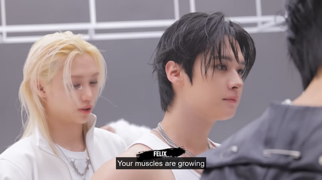 Felix stands behind Lee Know, looking appreciatively at his back, and says, 'Your muscles are growing.'