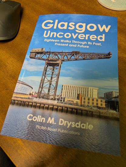 A book entitled 'Glasgow Uncovered: Eighteen Walks Through Its Past, Present and Future' by Colin M. Drysdale. The cover picture is a view across the river Clyde with a old ship-loading crane on the bank in front of some modern buildings, below a blue sky.