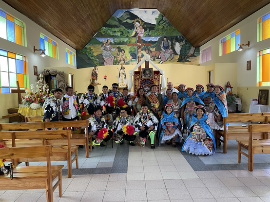 En el interior de una iglesia se vé el grupo de bailantes disfrazados con los mayordomos y el sacerdote
