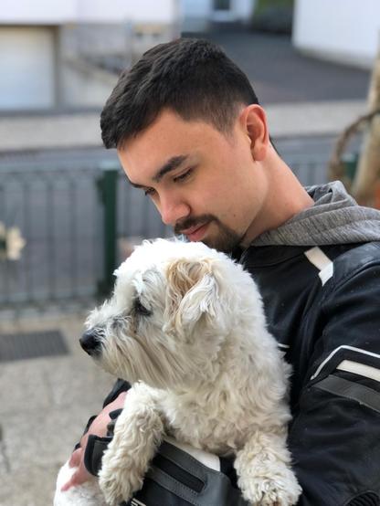 Brothers in arms ... junger Mann in Motorradkluft hält weißen, kleinen Hund in den Armen.
