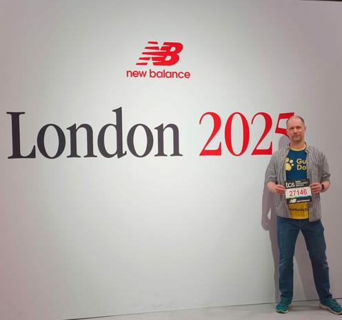 Me standing in front of a London 2025 logo wearing a Guide Dogs T-shirt and holding my race number.