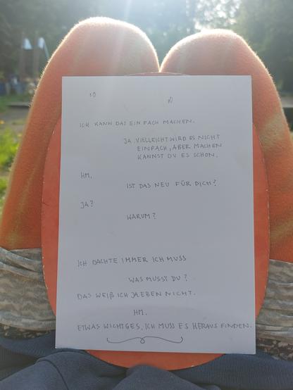 A photo taken outside, there is green gras in the back of the image. In the front is a paper with seemingly two entities exchanging in form of handwritten text:

Ich kann das einfach machen. 
Ja. Vielleicht wird es nicht einfach aber machen kannst du es schon. 
Hm.
Ist das neu für dich?
Ja?
Warum?
Ich dachte immer ich muss. 
Was musst du? 
Das weiß ich ja eben nicht.
Hm.
Etwas Wichtiges. Ich muss es heraus finden.