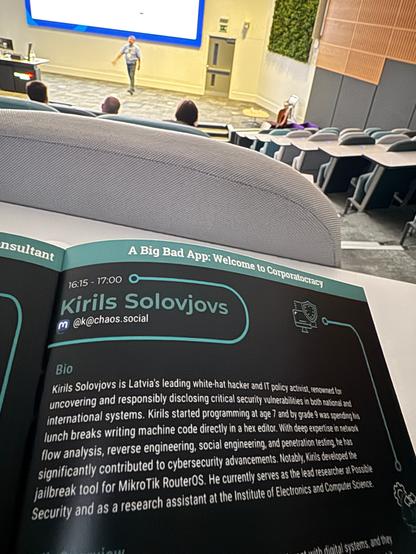 A lecture hall with a speaker and agensa on the bottom saying “Kirils Solovjovs”
