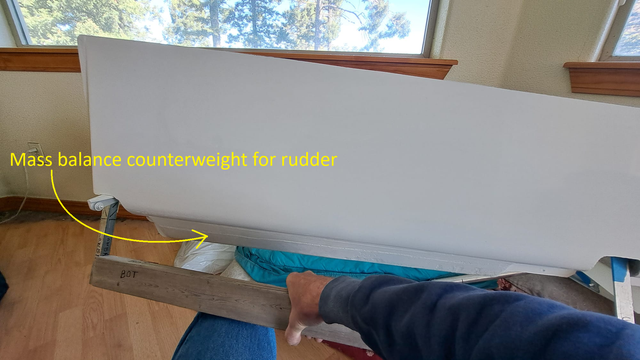 The rudder is free to pivot on this bracket.

The counterweight mass has shifted the center of gravity a bit forward of the pivot axis, so the trailing edge swings up and the counterweight swings to the bottom.

If there were no counterweight mass on this rudder, the trailing edge would drop to the lowest position. But this is not desirable, in terms of center of gravity location, to minimize vulnerability to flutter. So, we add the counterweight.

But how much mass? Enough to balance the rudder on the pivot axis in a static test?

Or do we need to consider other forces in a dynamic test? (See next photo....)