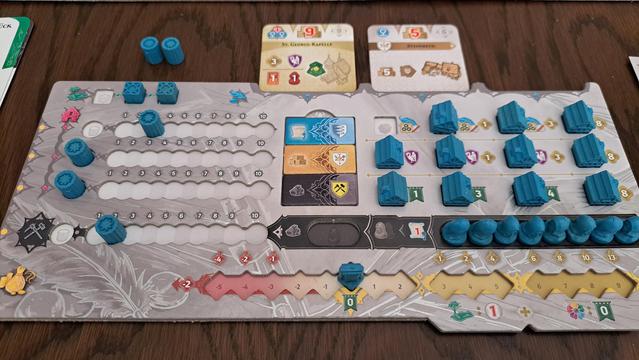 Blue player's double layer board with resource tracks for 3 guilds plus an ore track, wooden houses, and a reputation track. Above the board are two reserved building tiles.
